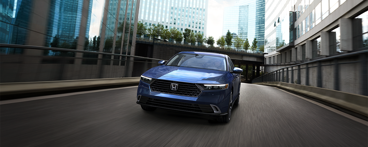 Front view of blue Accord drivign toward camera on an empty city street amid buidlings.