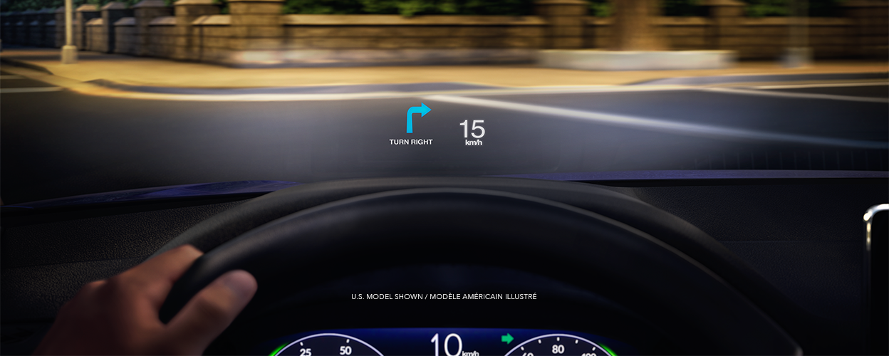 Point de vue du conducteur. Une projection sur le pare-brise affiche la vitesse et un clignotant alors que le conducteur se prépare à prendre un virage dans une rue urbaine tranquille la nuit.