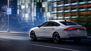 Plan de trois quarts arrière d’une Accord blanche circulant de nuit sur une autoroute devant des bâtiments. Des lignes de capteur bleues sont émises de l’avant et détectent un panneau routier.