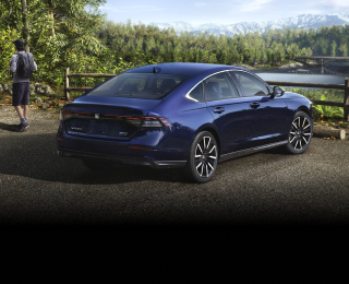 Plan de trois quarts arrière d’une Accord bleue stationnée avec vue sur une forêt et des montagnes. Un randonneur s’en éloigne.