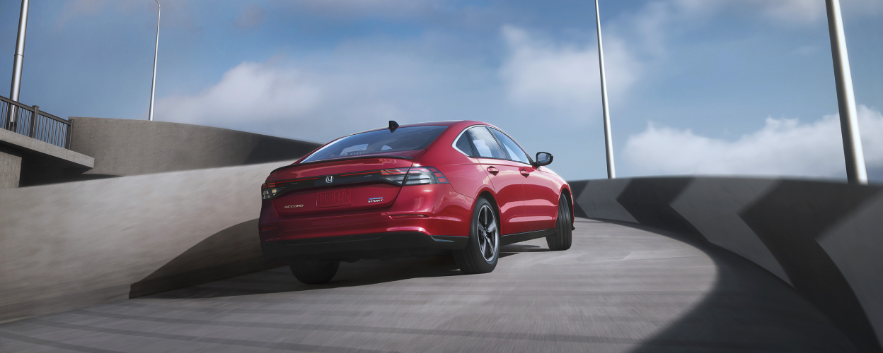 3/4 rear view of red Accord driving up the ramp of an outdoor parkade. 