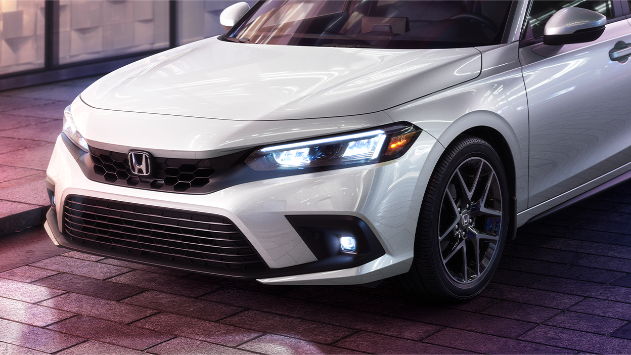 3/4 front view of a white Hatchback parked outside of a retail store, showcasing its headlights.