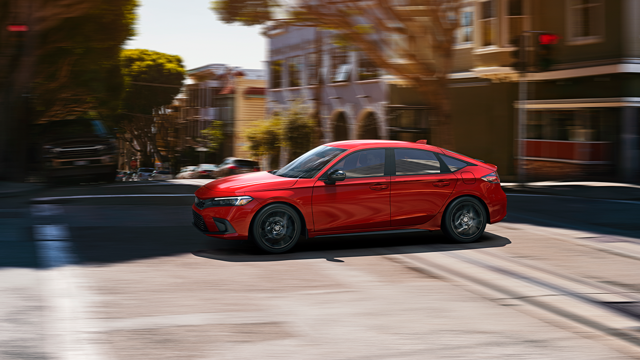 Sideview of red Hatchback driving on sunny city street.