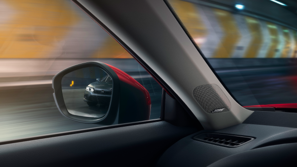 Interior closeup of the door mirror with the reflection of a car in it and a lit up blind spot indicator light.