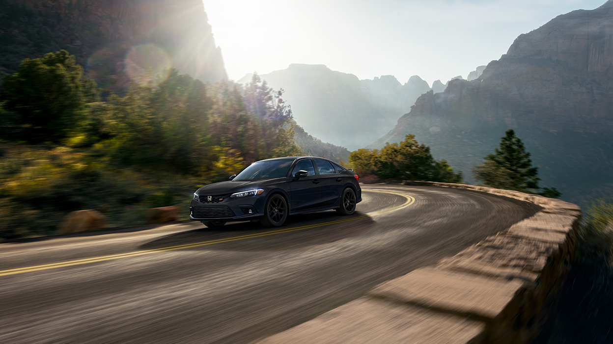 Vue latérale avant de trois quarts d’une Civic Si noire effectuant un virage sur une autoroute de montagne.