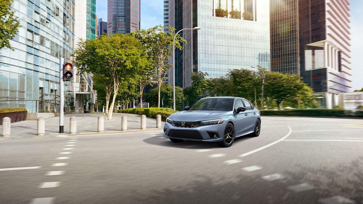 Vue avant de trois quarts d’une Civic Si gris-bleu effectuant un virage en ville avec beaucoup de verdure par une journée ensoleillée.