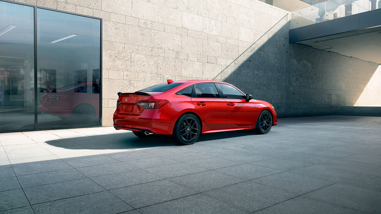 Rear sideview of a red Civic Si parked in front of a stone-walled building.