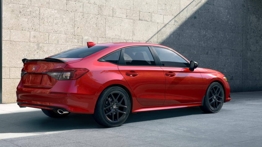 Plan latéral arrière d’une Civic Si rouge stationnée devant un bâtiment en pierres.