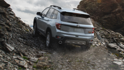 3/4 rear view of grey Passport driving up dirt road.
