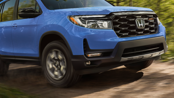 3/4 side front view, showcasing the front wheel on a blue Passport TrailSport as it drives on a dirt forest road. 