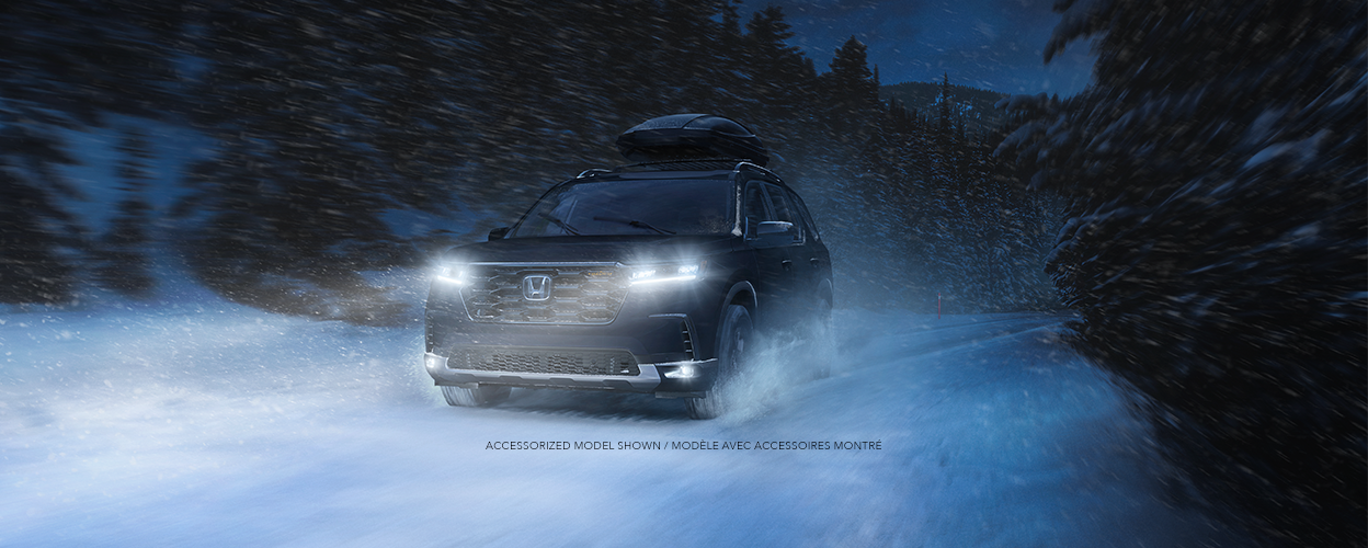 3/4 front view of black Pilot blasting through snow on a snowy forest road.