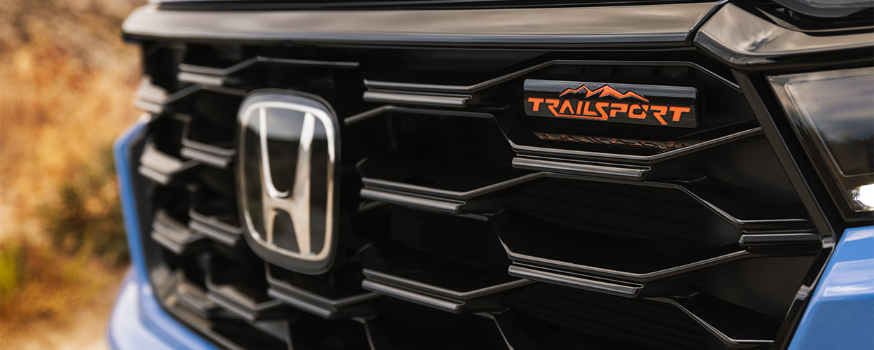 Closeup of front grille on light blue Pilot, showcasing the Honda logo and the TrailSport emblem.