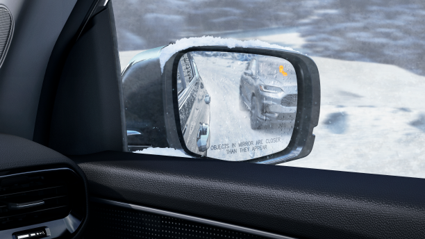 View of door mirror, seen from inside, showing a vehicle in the reflection and an illuminated alert light.