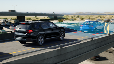 3/4 rear view of black Pilot on highway over pass. Blue sensor lines and waves detect the car in front. 