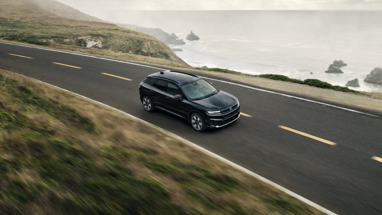 3/4 bird’s eye side view of black Prologue driving along a coastal highway.