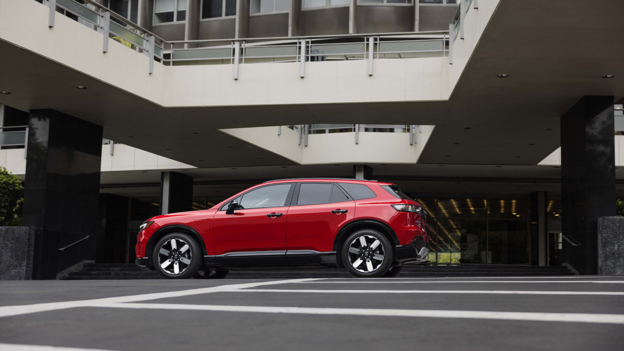 Wide side view of red Prologue parked in the driveway of a hotel-type building.