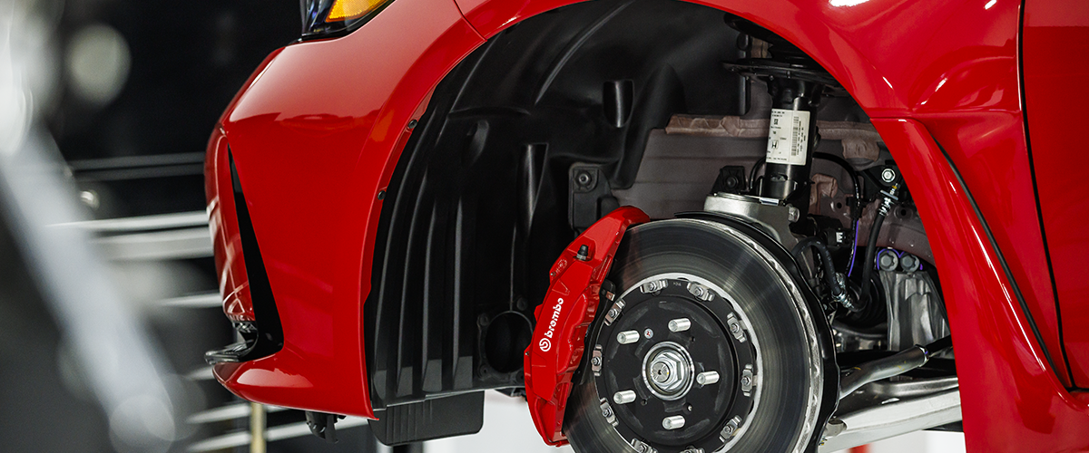 Closeup of disc brake and Brembo® caliper on red Type R on a lift in a garage.